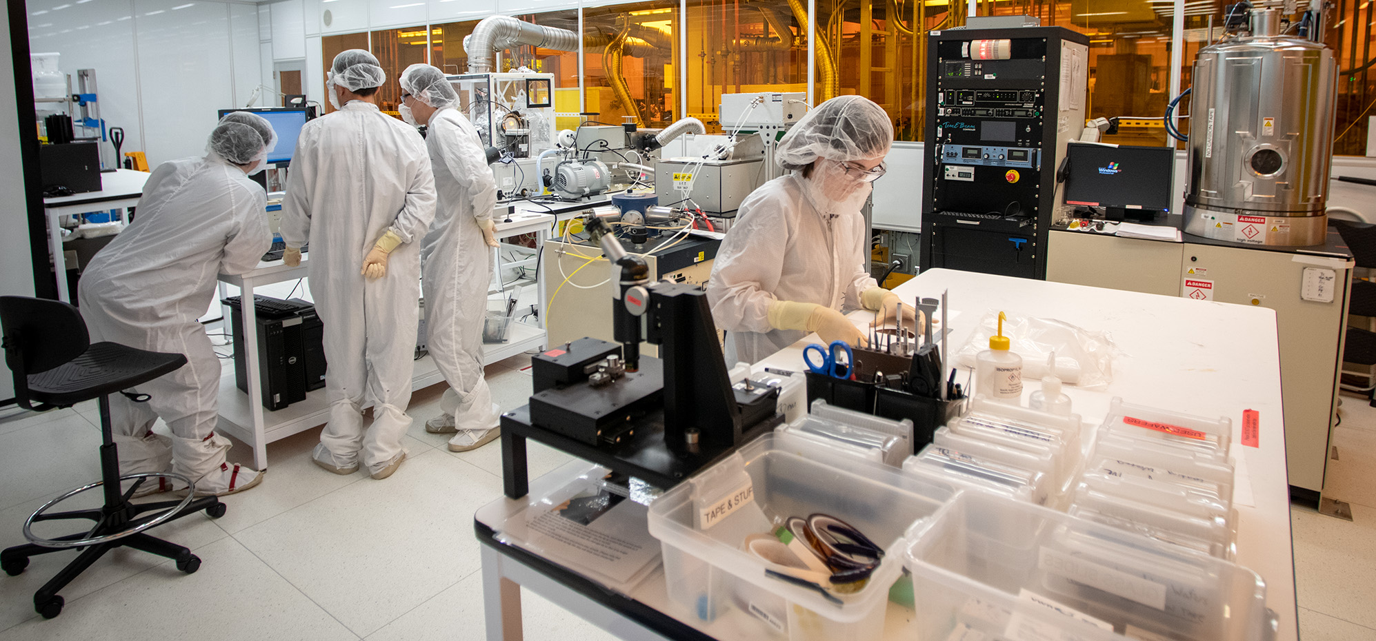 A clean room with employees working at workstations on the left, a work table in the center with an employee looking down at a sample.