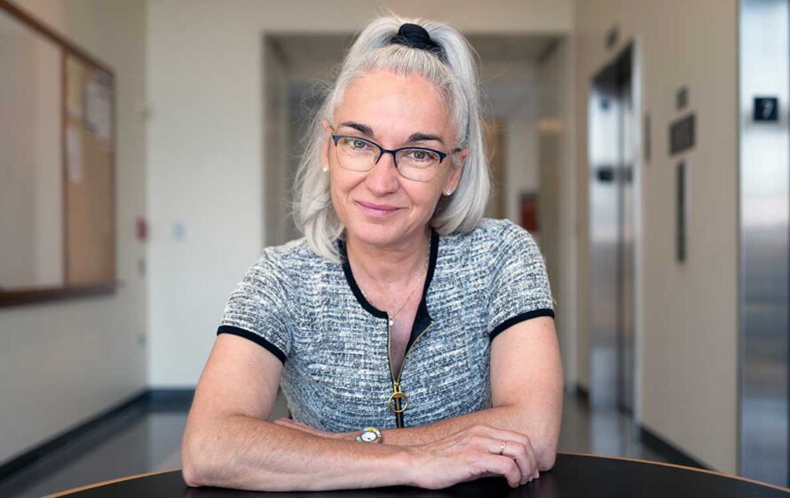 Eva Nogales smiling with forearms propped on a round table in a cream-toned hallway of Stanley Hall on the UC Berkeley campus.