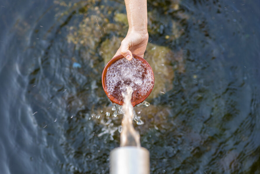 Outstretched hand holding a bowl collecting natrual water.