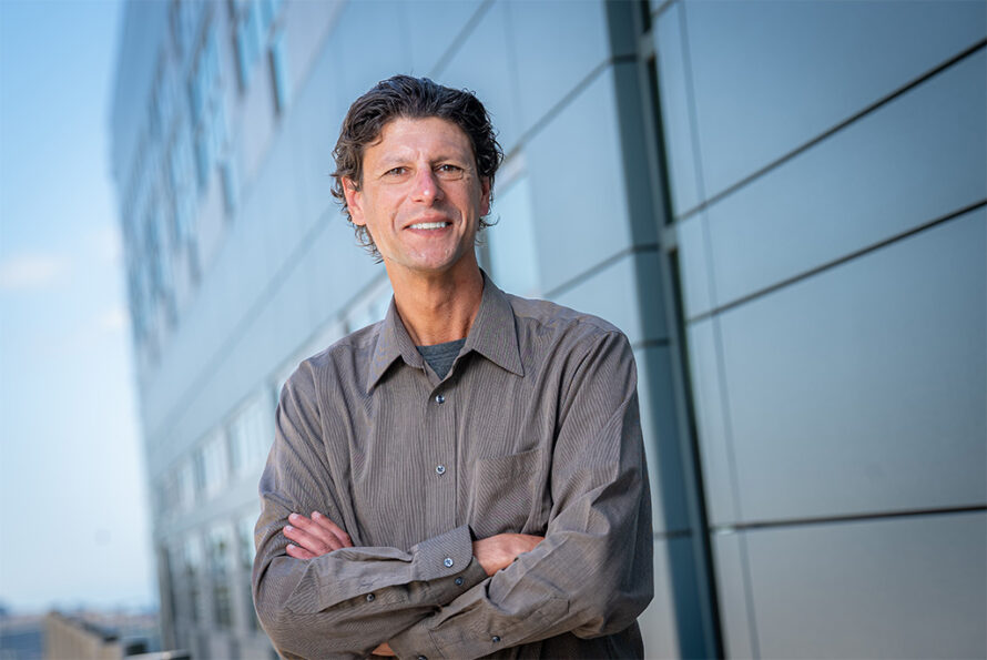 Man smiling at camera in front of a building and blue sky.