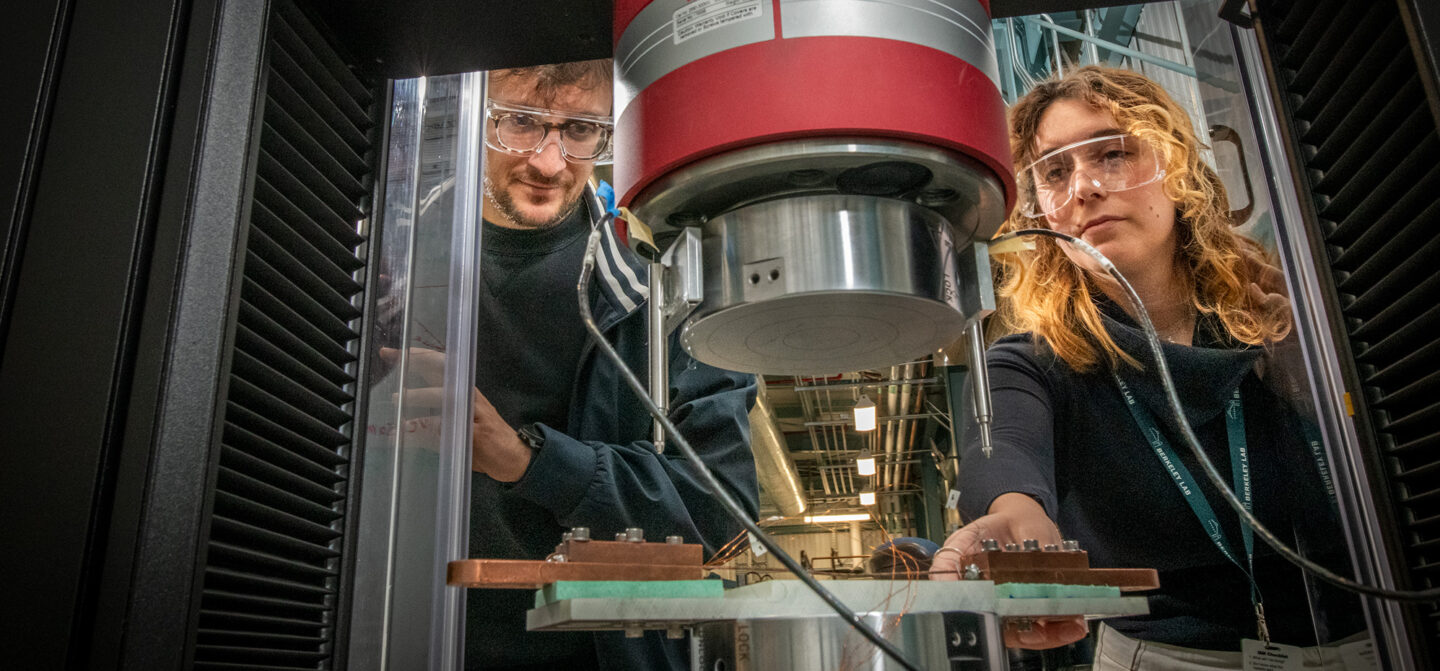 Two researchers in protective glasses look into a superconducting magnet experimental setup.