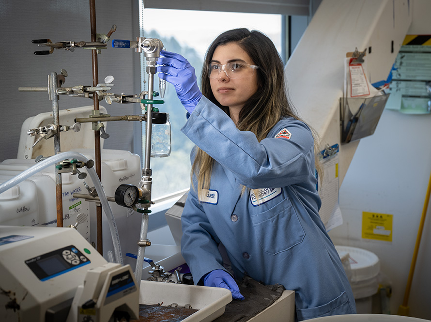 A researcher wearing glasses and a blue lab coat works in a lab and adjusts a titration.