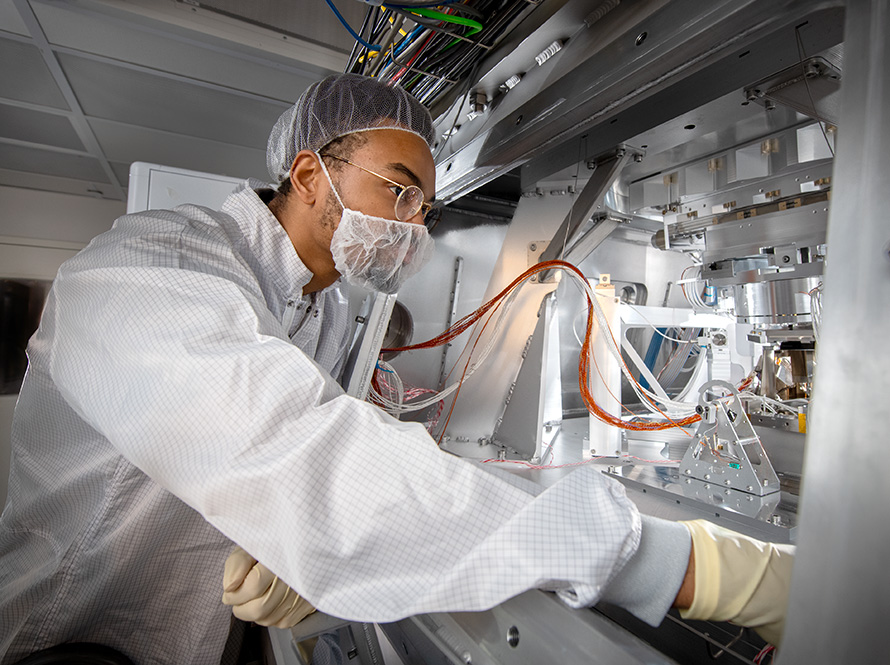 A researcher dressed in personal protective equipment operates a machine.