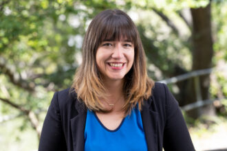 Person with shoulder-length hair with blue shirt and black sweater