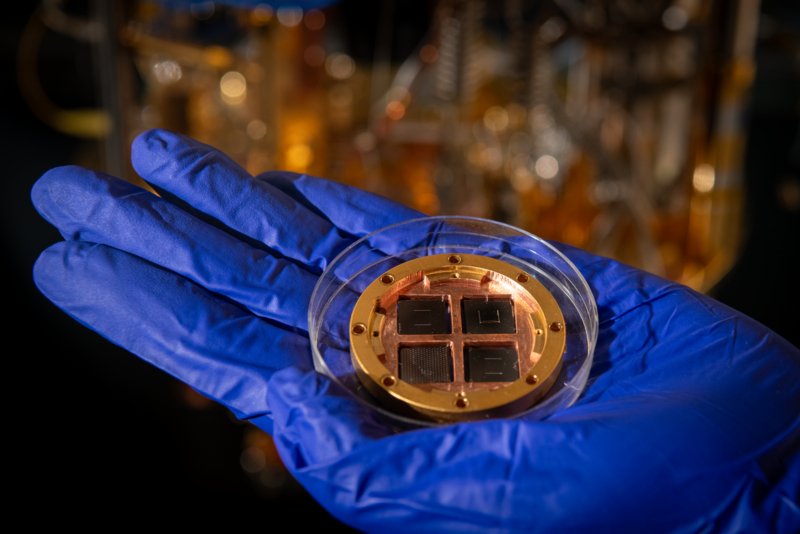 Hand wearing blue glove holding gold-colored component