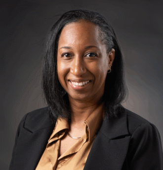 Person wearing a tan collared shirt and black blazer