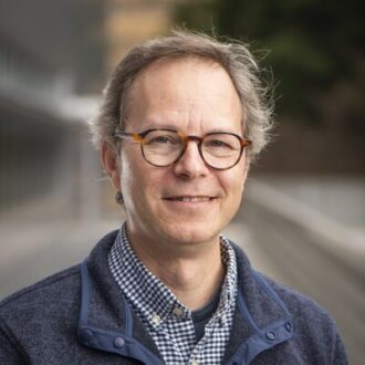 Person wearing glasses, blue collared shirt and blue outerjacket
