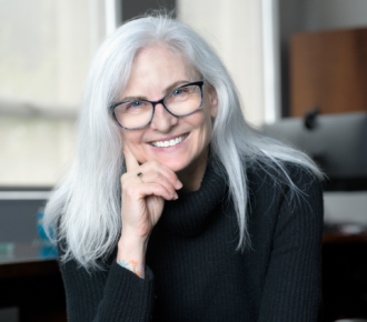 Person with black glasses, shoulder length silver hair, and a black sweater