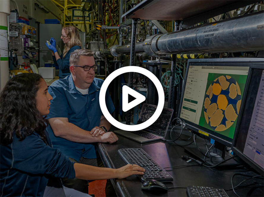 Three researchers dressed in blue-colored office clothes analyzing microtomography computer images of an orange-colored material sample in a lab.