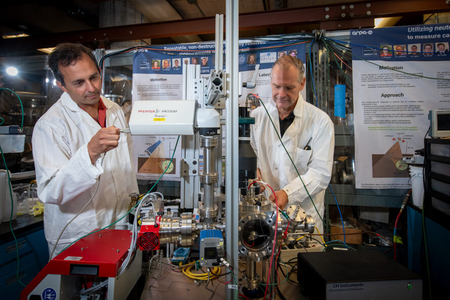 Two people in lab coats adjust equipment.