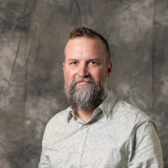 Person with facial hair wearing collared shirt against gray background