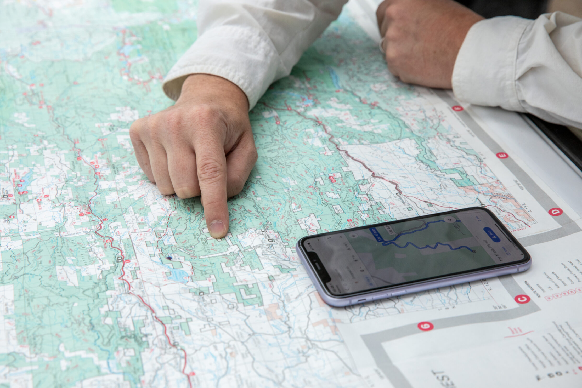 Person's hand on top of a map with a smartphone next to it