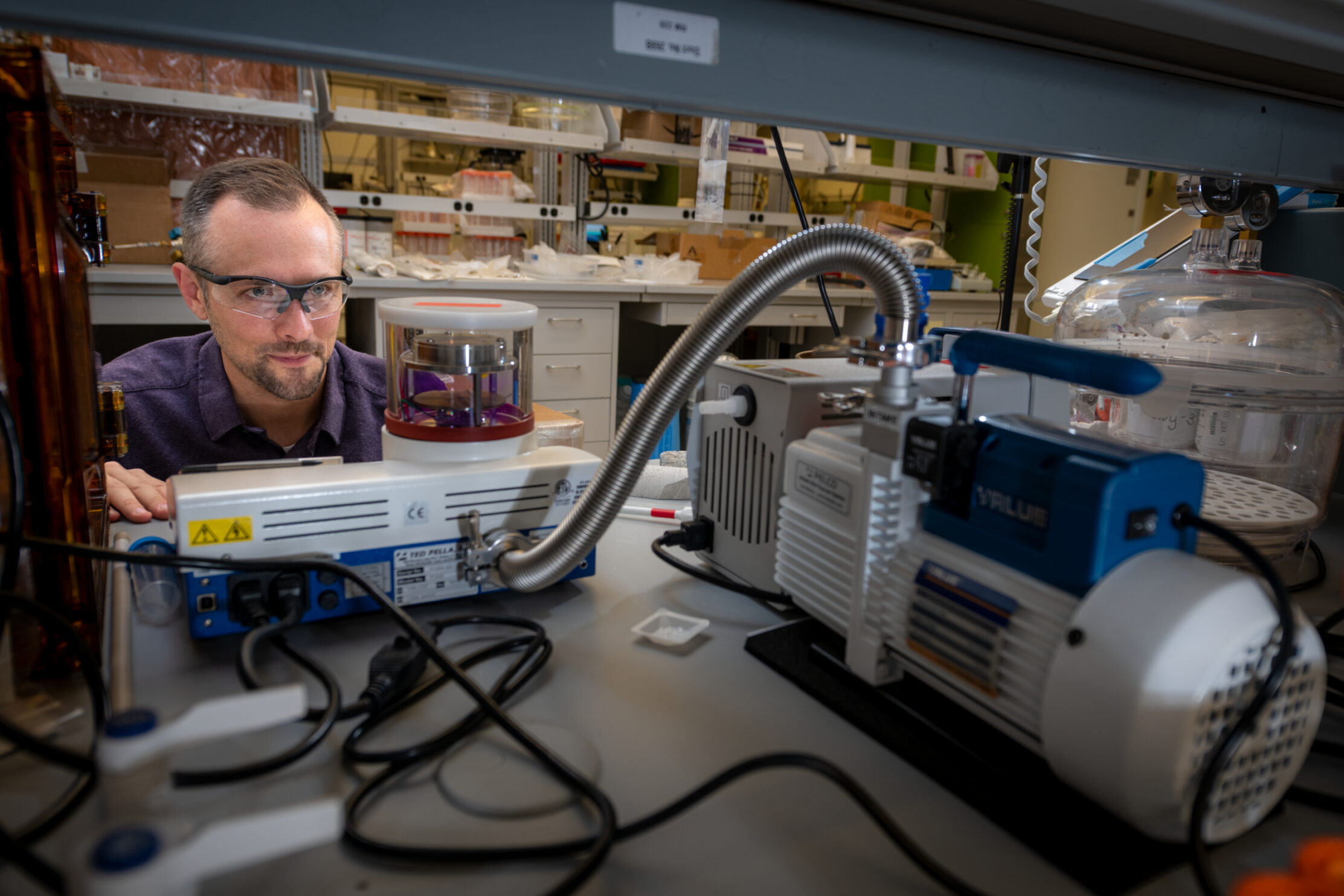 Person wearing glasses looking at sample in lab machinery